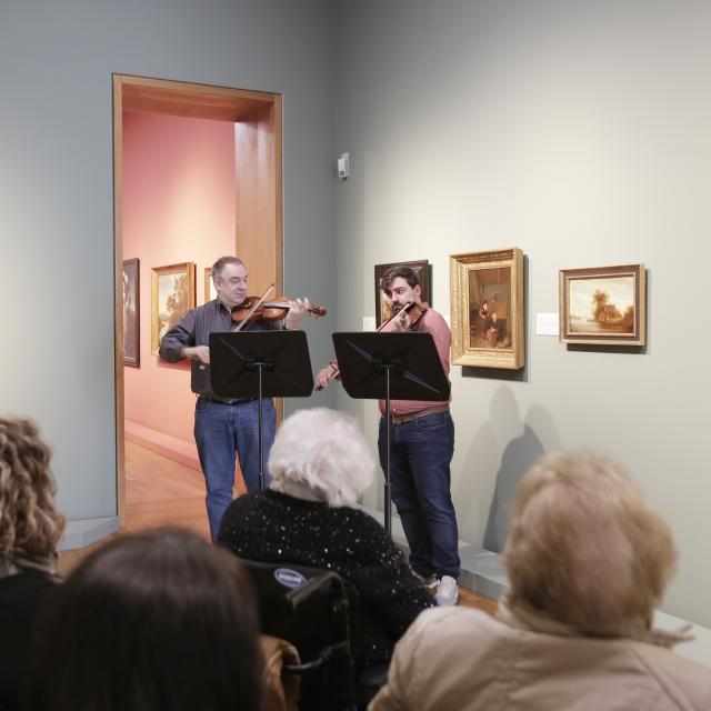 Deux violonistes jouant devant des personnes assises dans un musée