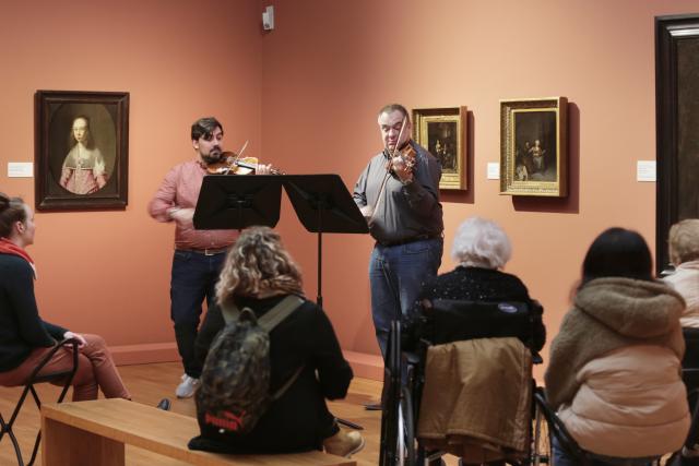 Deux violinistes jouant devant un groupe de personnes assises dans un musée