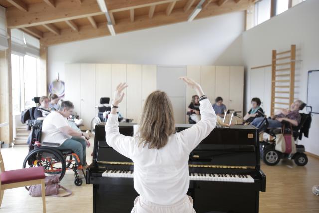 Une femme levant les bras devant un piano et des personnes en fauteuil roulant en arrière-plan