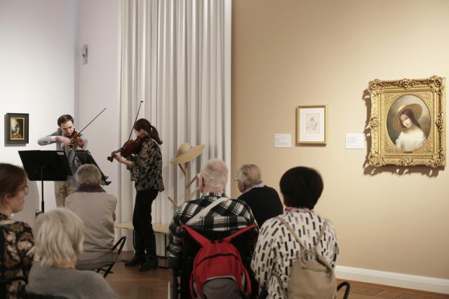 Deux violinistes jouant devant un groupe de personnes assises dans un musée