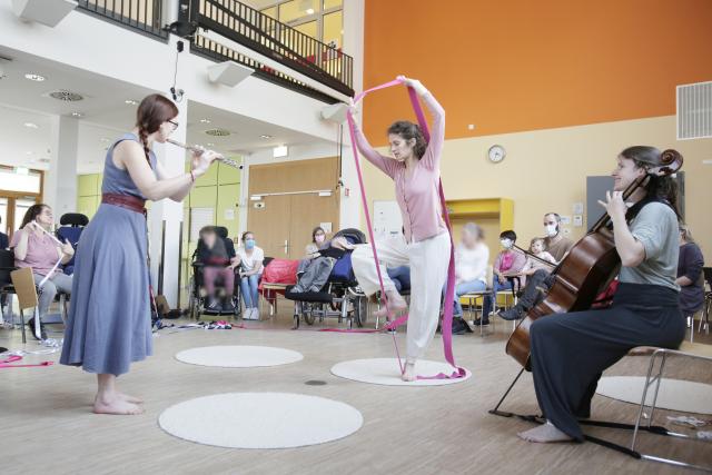 Two women dancing together with arms raised and a cellist playing music