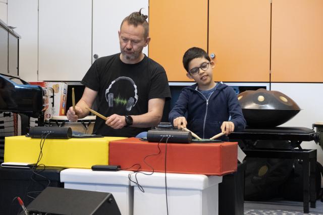 Un artiste et un jeune garçon jouant sur des batteries électriques côte à côte