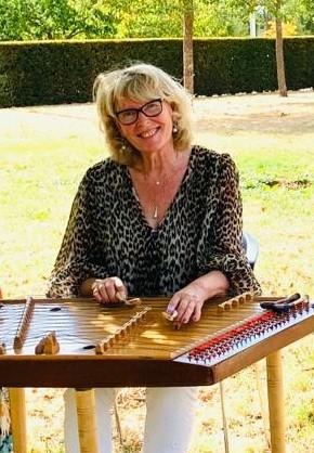 Eine frontal sitzende, lächelnde Frau, die ein Cimbalom spielt