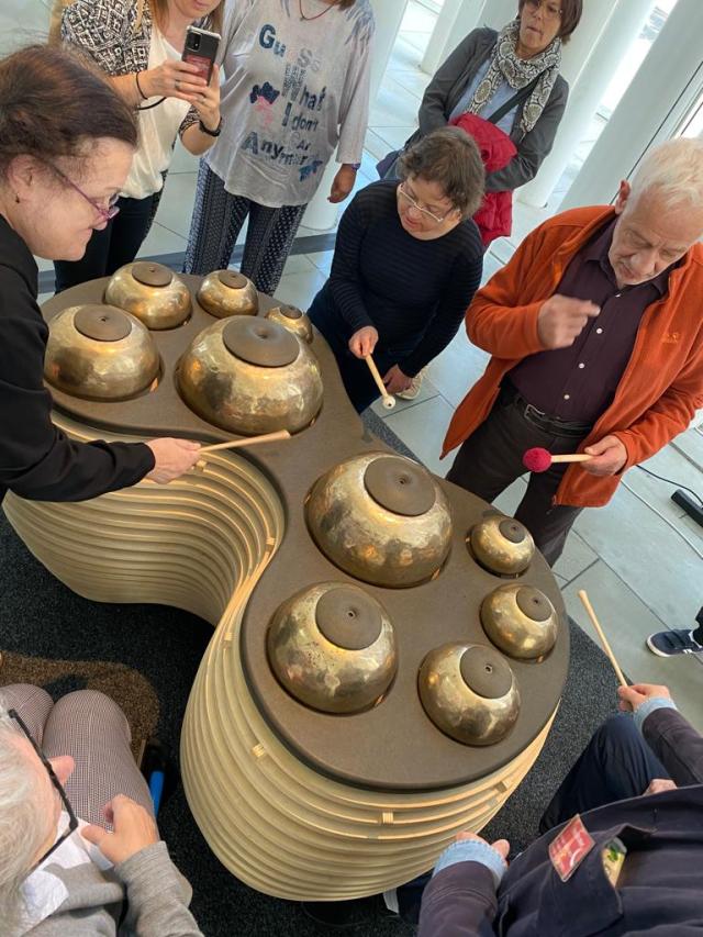 Un groupe de personnes rassemblées autour d'un instrument métallique et tappant dessus avec des baguettes de batterie