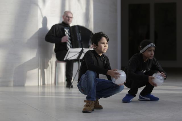 Deux enfants accroupis avec un ballon devant un accordéoniste