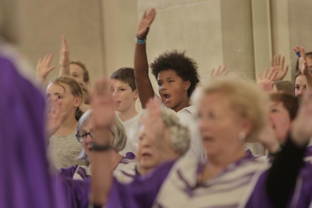 Des personnes âgées en robe violette chant avec des jeunes situés derrière eux