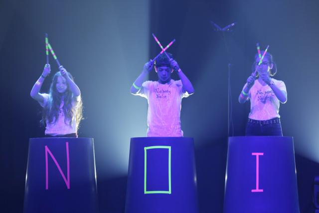 Des jeunes derrière un décor avec les lettres "N, O et I" et faisant un "X" avec des baguettes