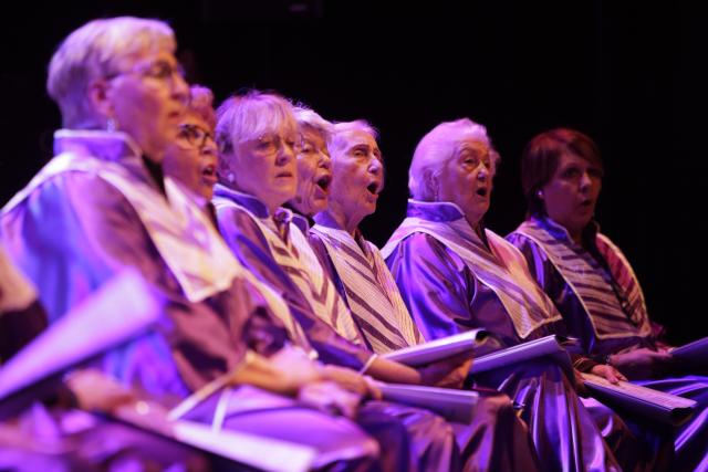 Des personnes âgées en robe violette chantant sur scène