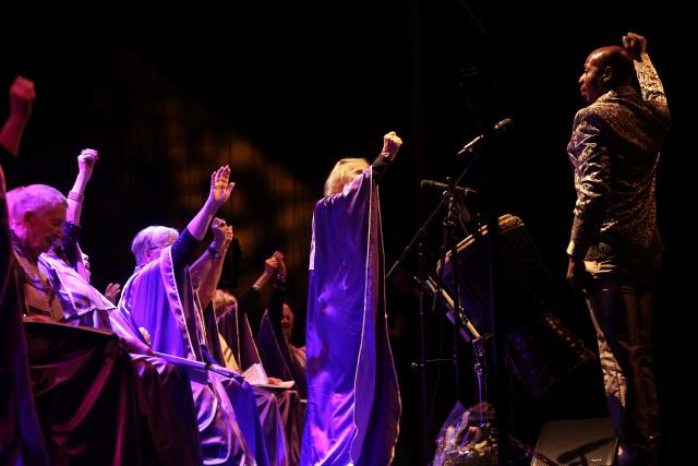 Des personnes en robe violette levant le poing sur scène