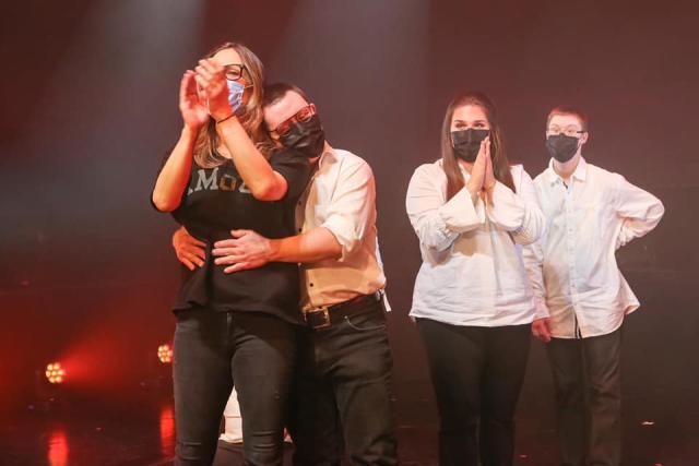 Une personne prenant une autre personne dans ses bras et deux personnes se tenant debout à côté