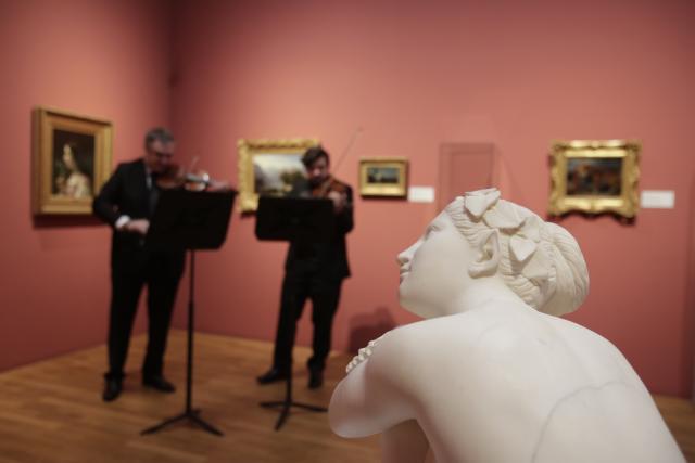 Deux violonistes jouant devant des tableaux et une statue au premier-plan