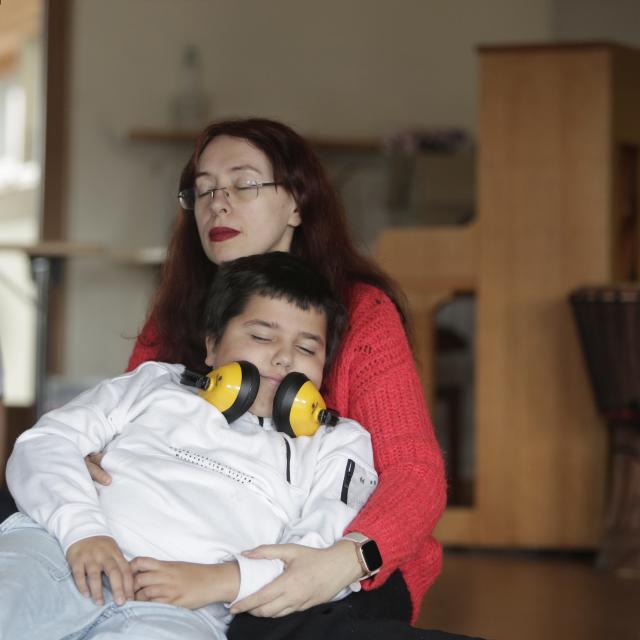 Un enfant avec un casque autour du cou endormi contre une adulte fermant les yeux