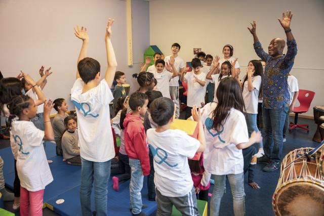 Des enfants rassemblés autour d'un percussioniste levant tous les bras