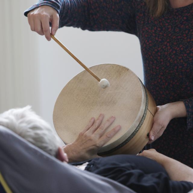 Une musicienne montrant à une personne allongée comment tapper sur un tambourin