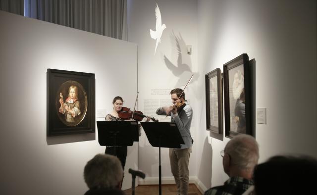 Deux violinistes jouant devant un groupe de personnes assises dans un musée