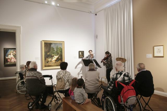 Deux violinistes jouant devant un groupe de personnes assises dans un musée