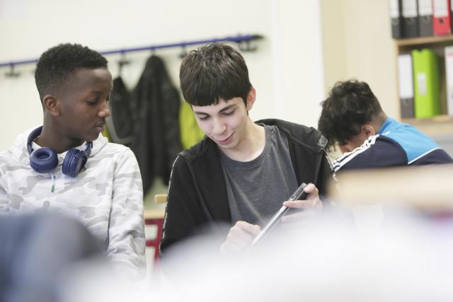 Un élève tourant l'écran de sa tablette vers un autre élève et lui montrant des choses en souriant