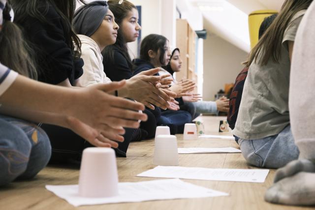 Un groupe d'enfants assis frappant dans leurs mains devant des verres en plastiques retournés et posés au sol