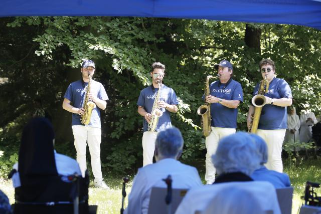 4 saxophonistes debout devant des personnes âgées assises