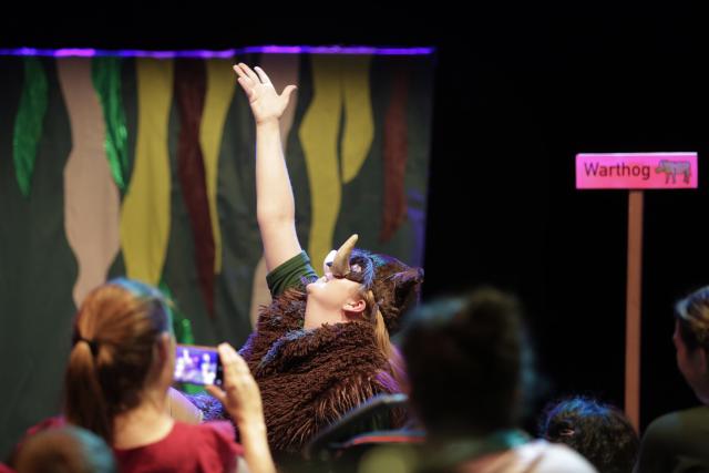 Une artiste déguisée en phacochère levant son bras droit