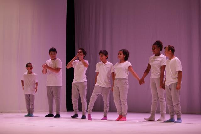 Des enfants debout sur scène dans une ambiance lumineuse rose