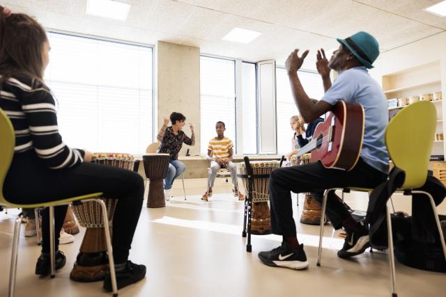 Un groupe d'enfants jouant du djembé ensemble et un homme avec une guitare frappant dans ses mains