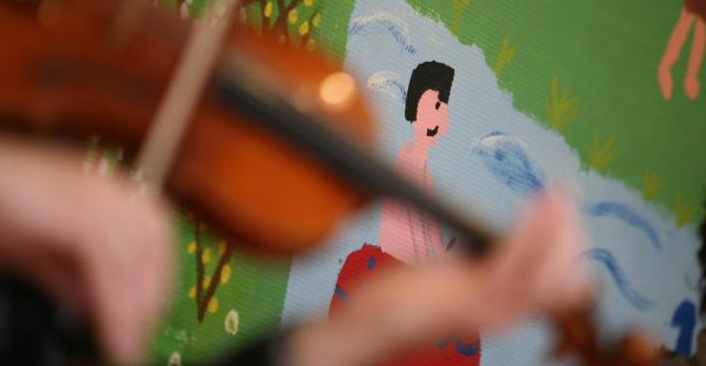 Une personne jouant du violon devant un mur peint par des enfants