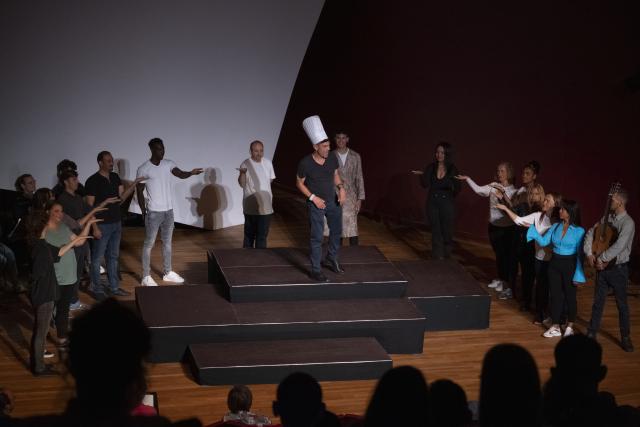 Des personnes rassemblées autour d'un homme porant une toque de chef cuisinier au centre de la scène