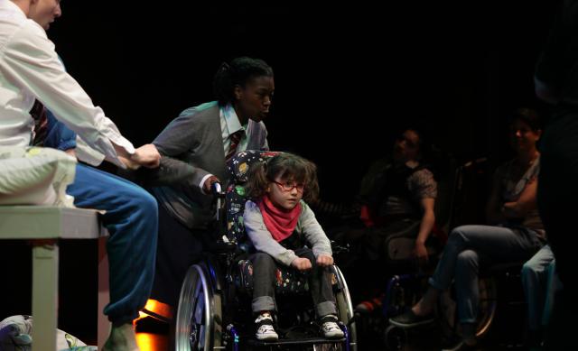 Un enfant en fauteuil roulant sur scène, au milieu des artistes