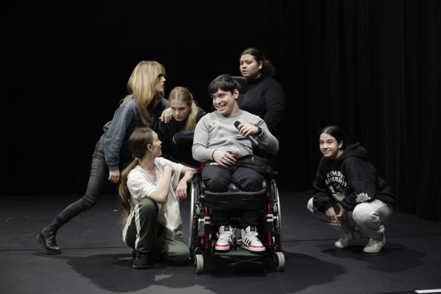 Des personnes sur scène regroupées autour d'un jeune en fauteuil roulant tenant un microphone