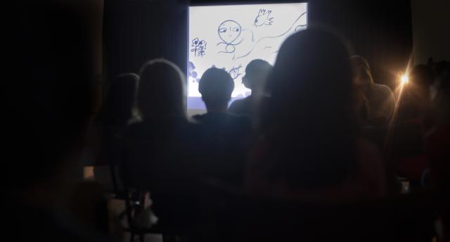 Des enfants de dos regardant des dessins projetés sur scène